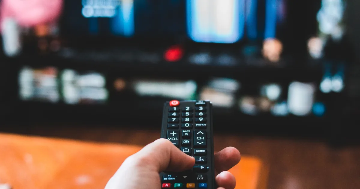 Person holding a television remote toward a TV in a living room setup