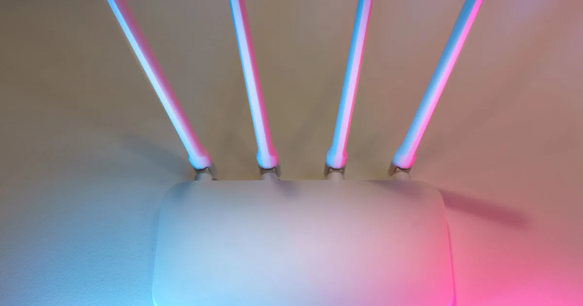 White wireless router with four antennas lit by blue and pink light