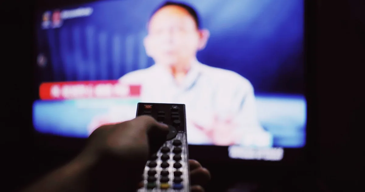 Hand holding a remote control toward a television in a dim living room